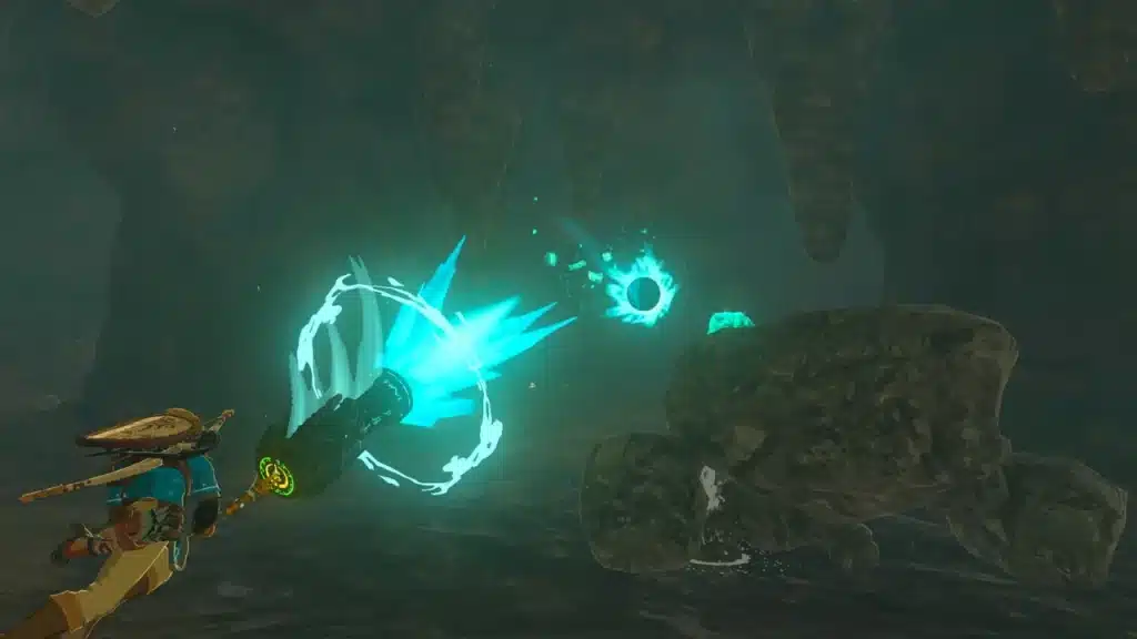 Link swinging a glowing fused weapon at rocks in a dark cave in Tears of the Kingdom