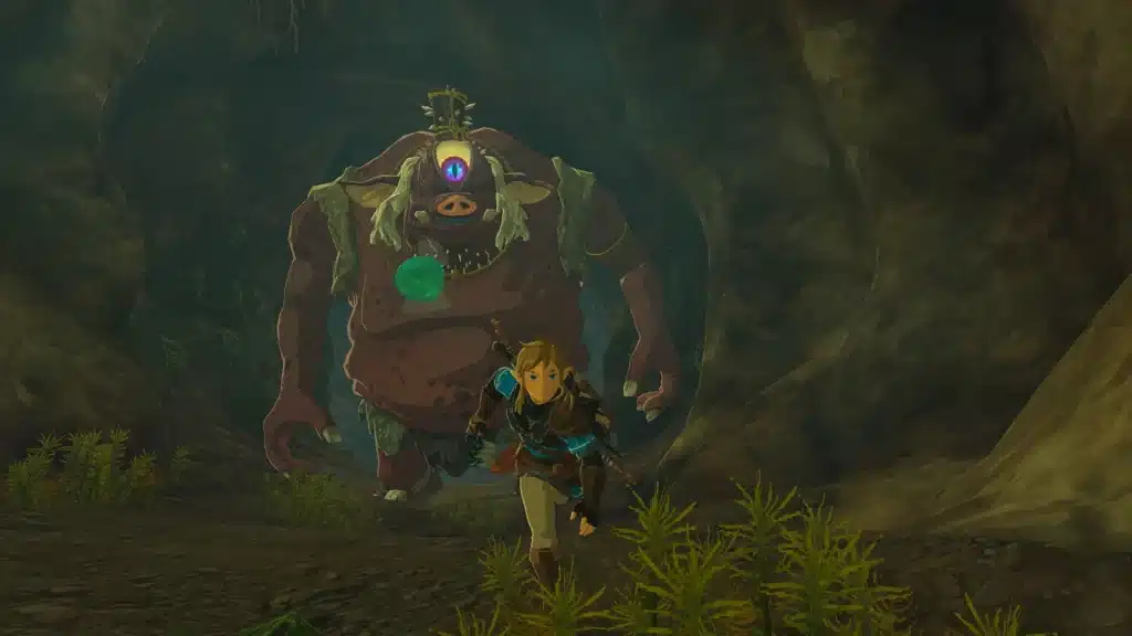 Link running through a dark cave in Tears of the Kingdom with a one-eyed Hinox close behind